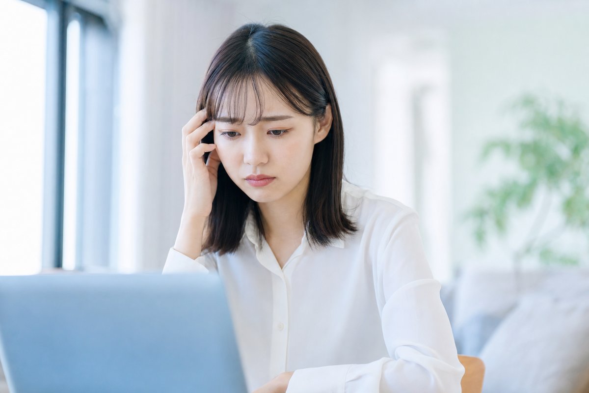 20代後半の女性が自席でパソコンの前に座り、退職の話を切り出せず視線を落として不安げな表情をしている