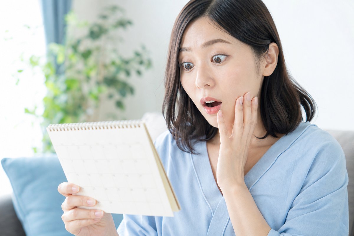 30代の女性が自宅でカレンダーを確認しながら、認定日をうっかり忘れていたことに気づき驚いた表情を浮かべている
