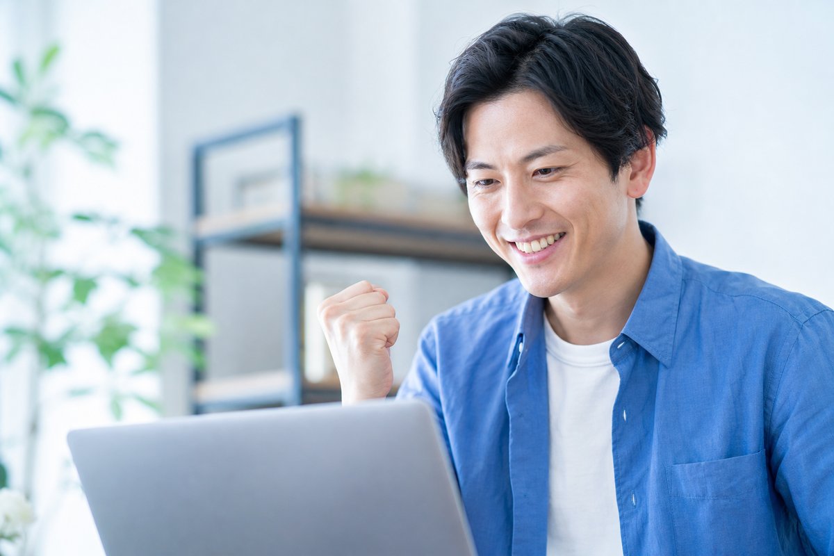 30代の男性がノートパソコンの前で笑顔になり、安心した表情で軽くガッツポーズをしている