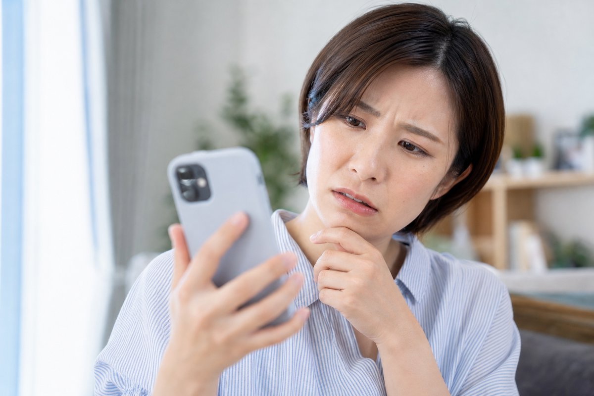 30代の女性が自宅でスマートフォンの受給資格者証の写真を見ながら、眉を寄せて次回の認定日を確認し困った表情をしている