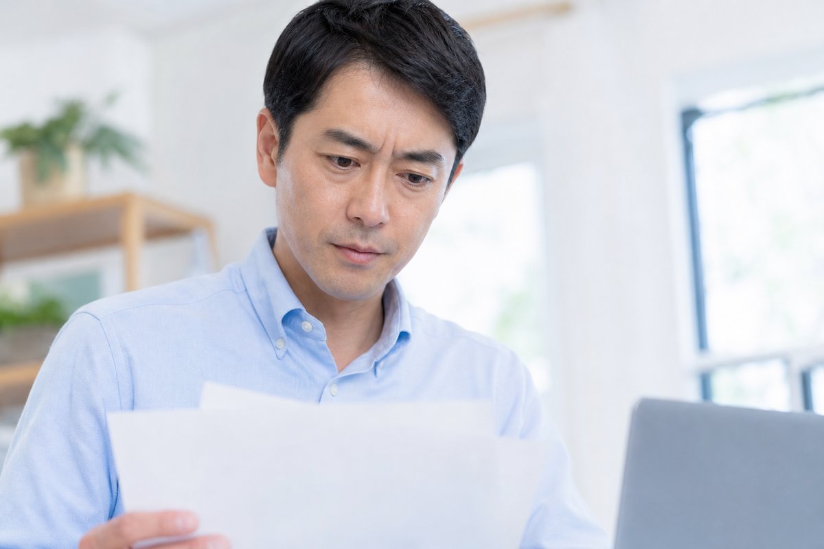 40代の男性がデスクで書類を手に取り、真剣な表情で条件を確認している