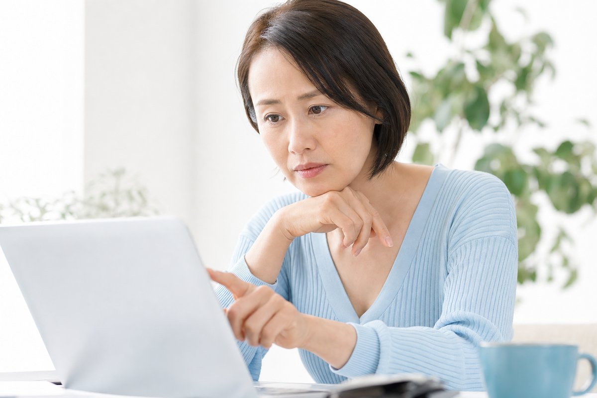 40代の女性がノートパソコンの画面を見ながら、保険料の見積もりを比較するように真剣な表情で指でなぞっている