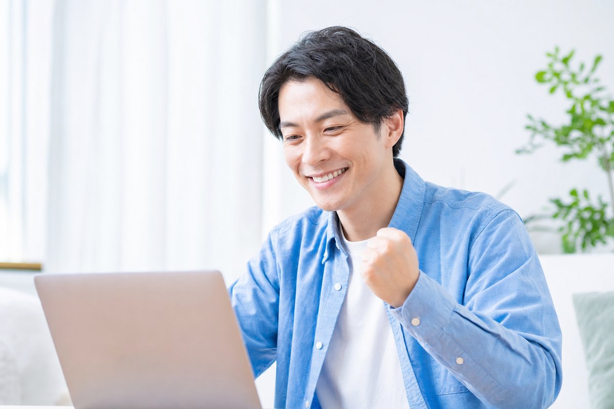 30代の男性がノートパソコンの前で笑顔になり、安心した表情で軽くガッツポーズをしている