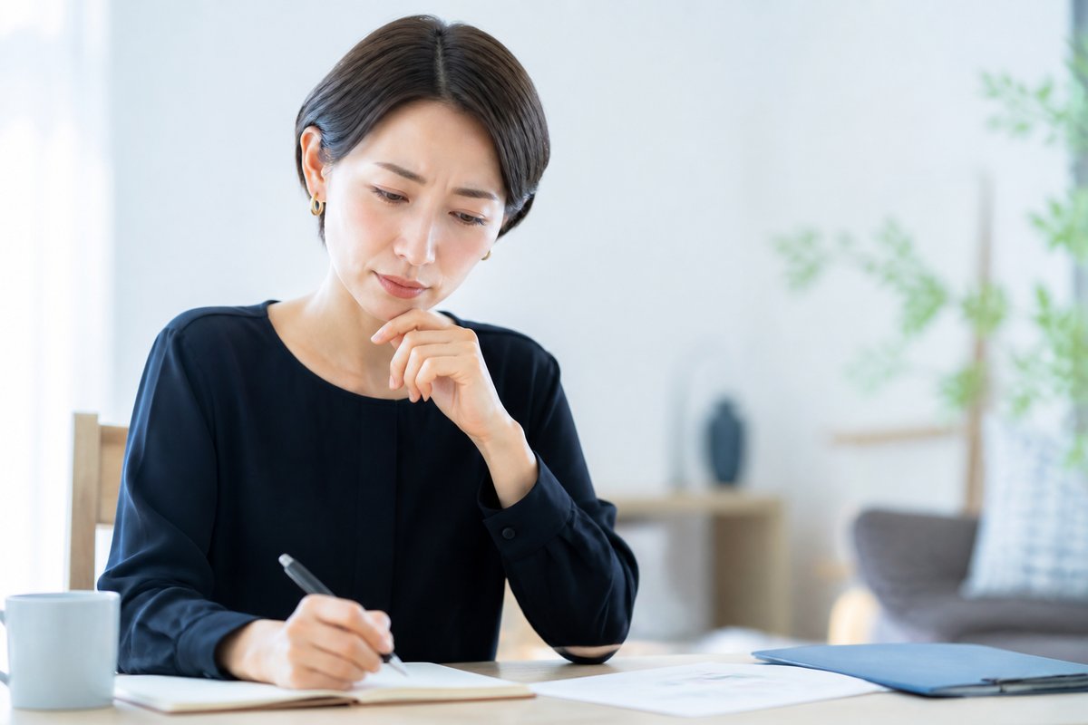 30代の女性がノートに書き込みながら、考え込むような真剣な表情をしている