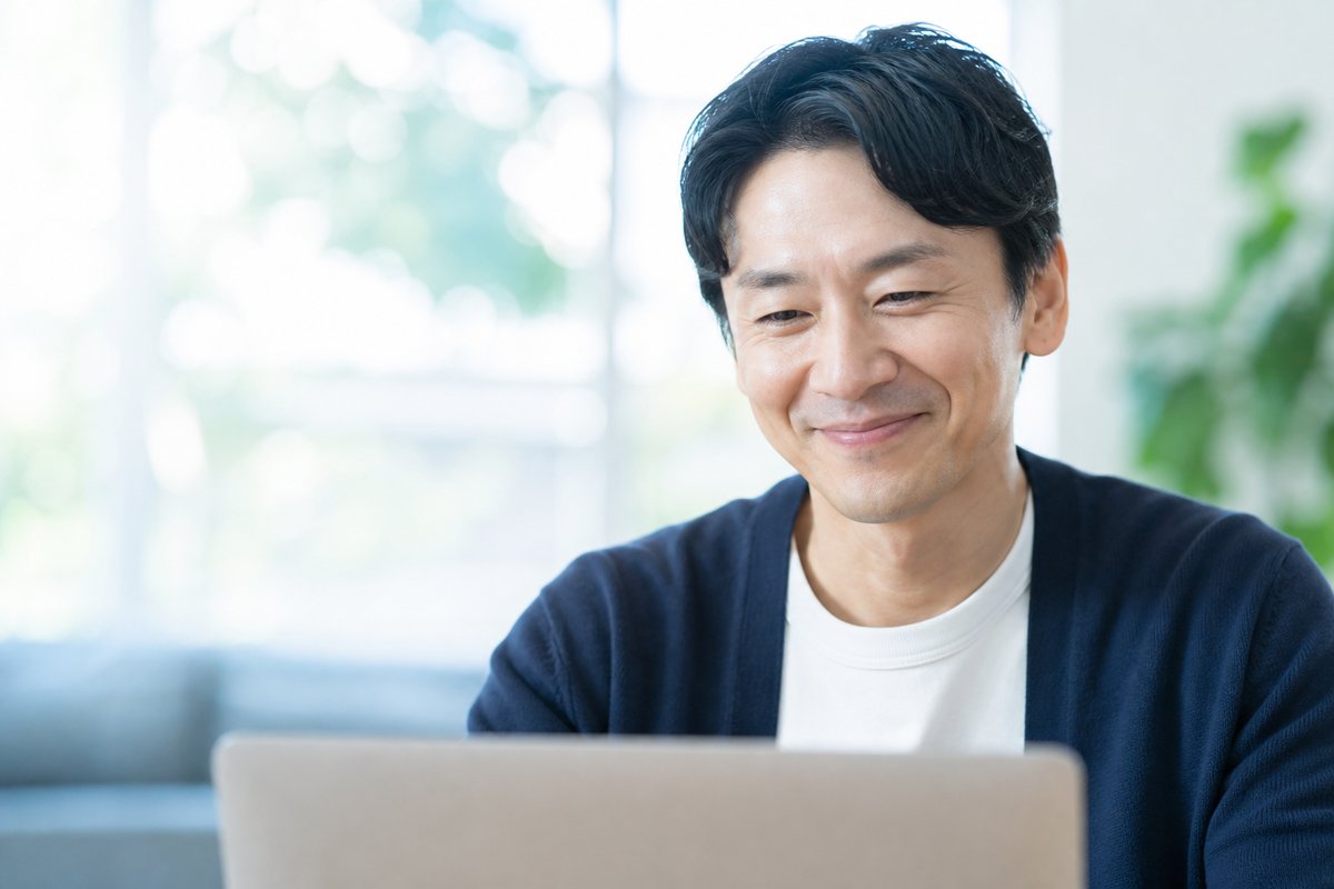 40代の男性がノートパソコンの前で笑顔になり、安心した表情でうなずいている