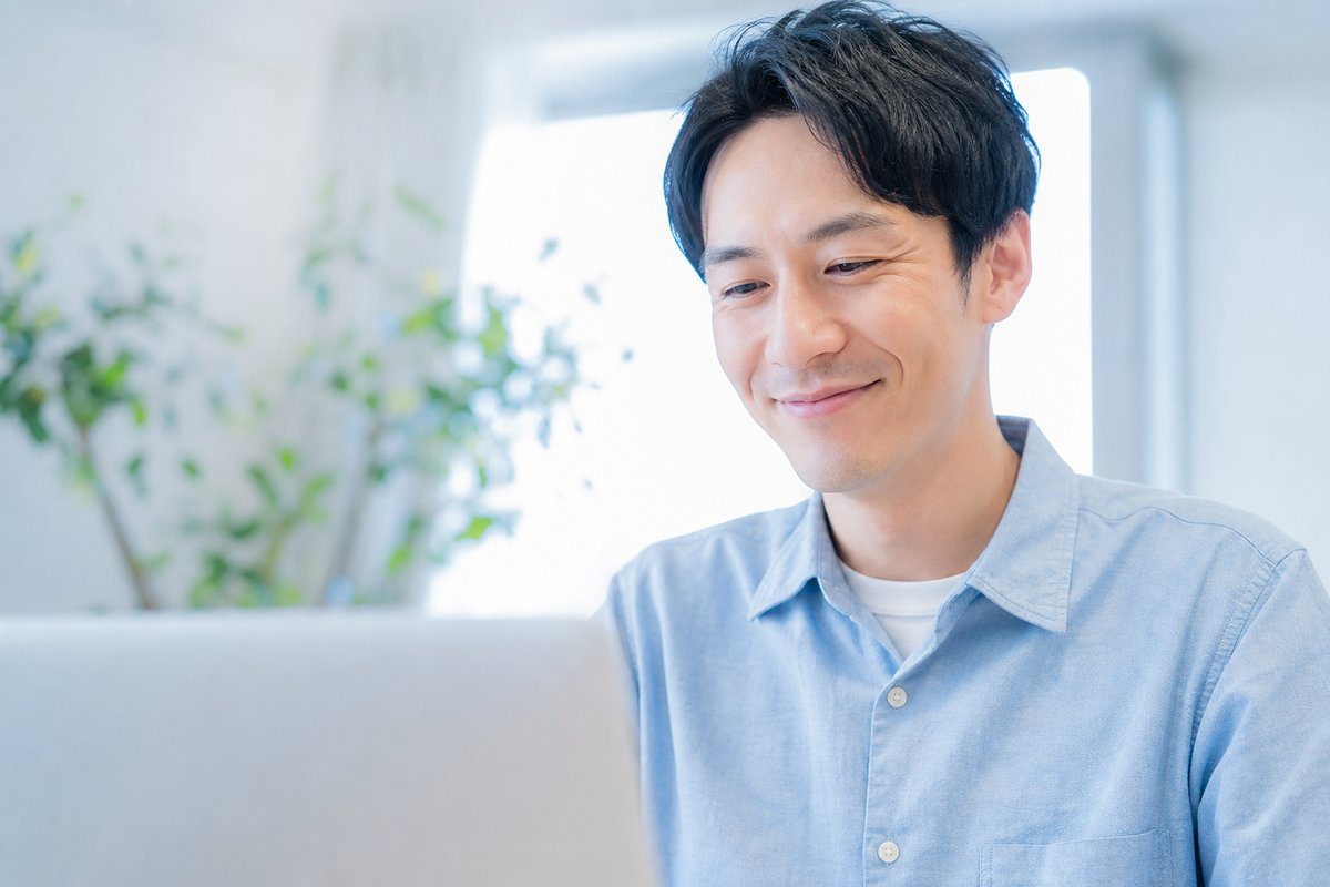 30代の男性がノートパソコンの前で笑顔になり、安心した表情で軽くうなずいている
