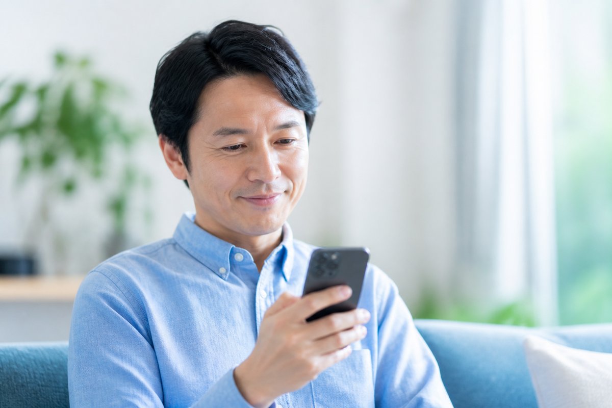 40代の男性がスマートフォンの画面を見ながら安心した表情になり、小さく笑みを浮かべている