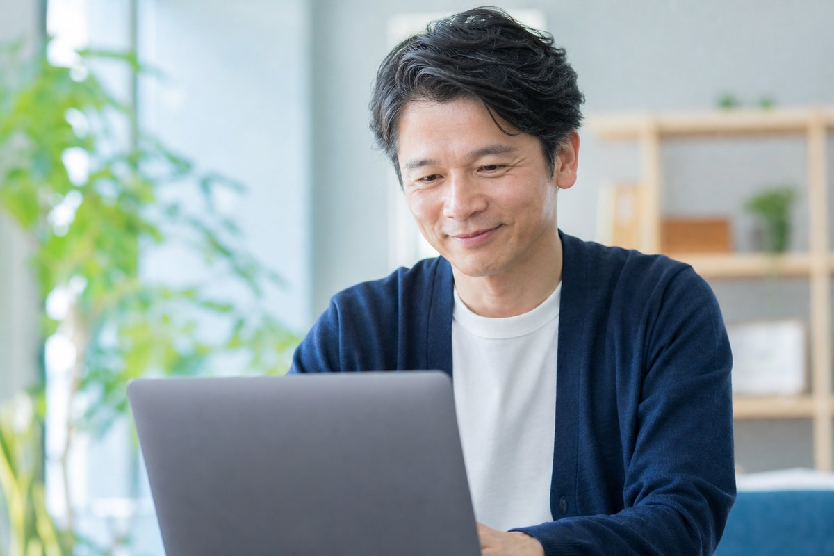 40代の男性がノートパソコンの前で笑顔になり、安心した表情で軽くうなずいている