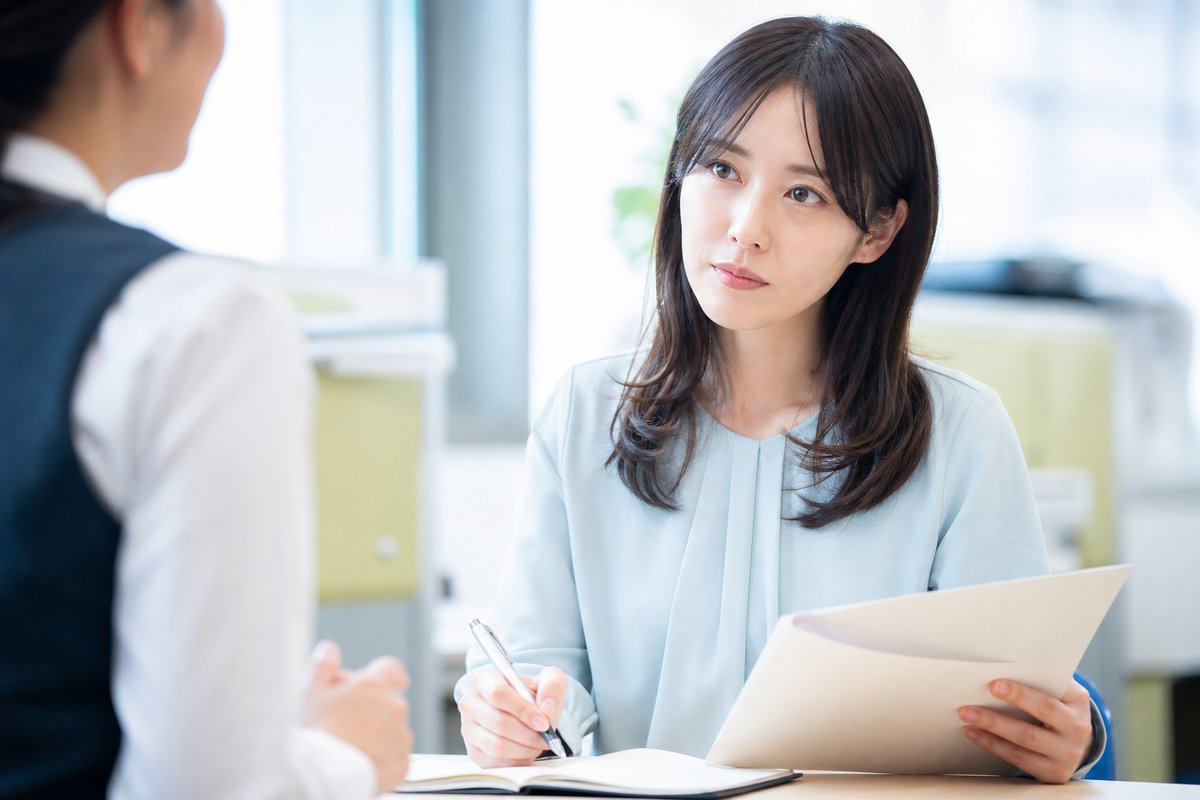 30代の女性が書類とノートを手にしながら、真剣な表情でハローワークの窓口担当者の説明を聞いてメモを取っている
