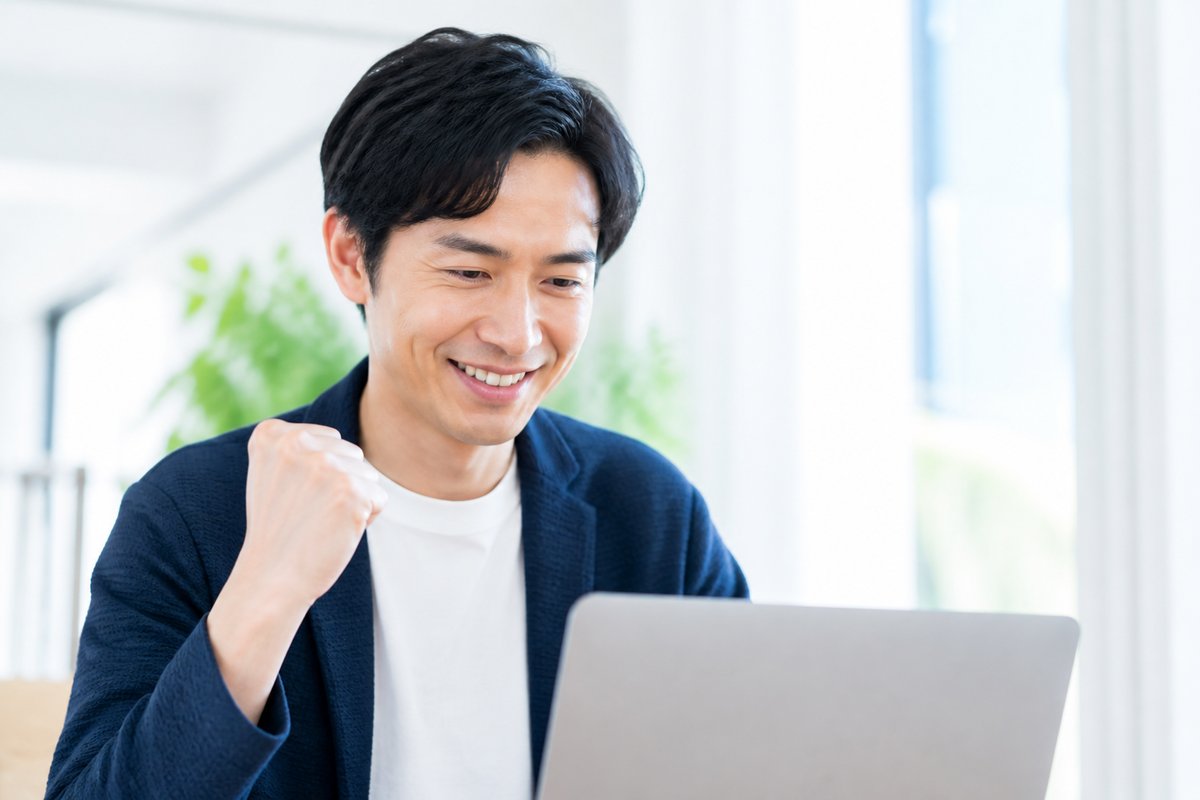 30代の男性がノートパソコンの前で笑顔になり、安心した表情で軽くガッツポーズをしている