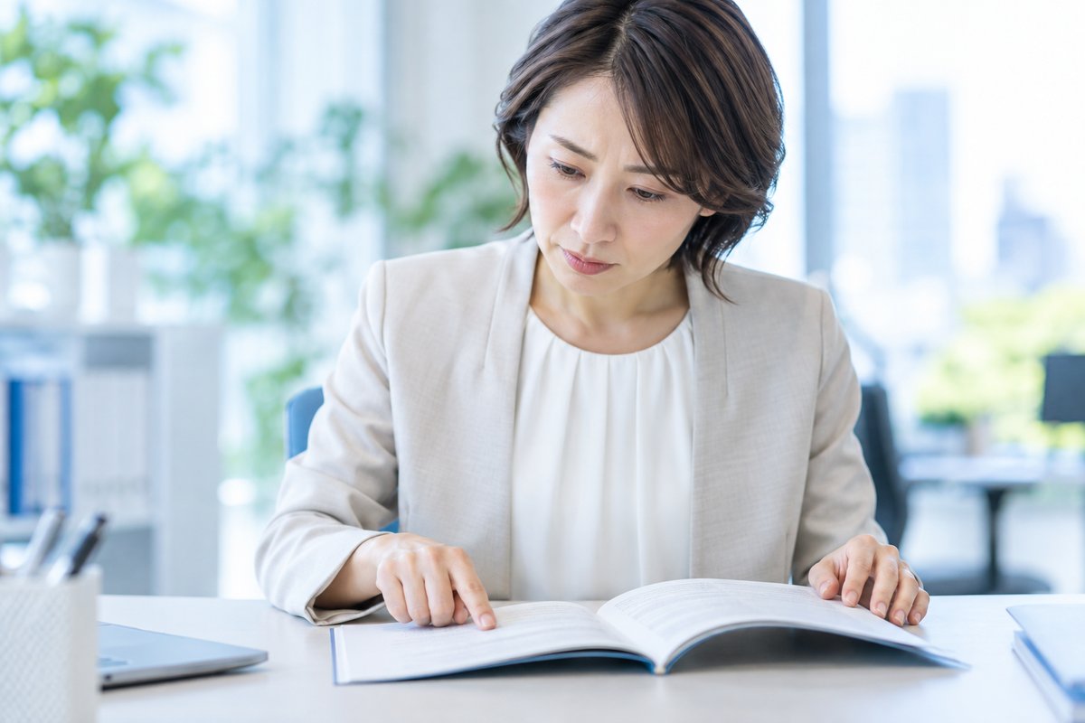 40代の女性がオフィスの席で就業規則の冊子を開き、支給日の記載を指でたどりながら真剣な表情で確認している