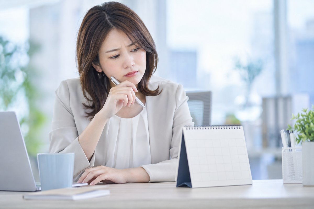 30代の女性がオフィスの自席でカレンダーを見ながら、眉を寄せて引き継ぎの開始時期に迷っている表情を浮かべている