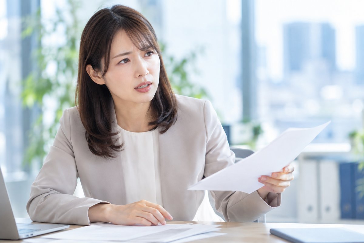 30代の女性社員が上司の男性に資料を見せながら、引き継ぎが間に合わない状況を相談して真剣に話している