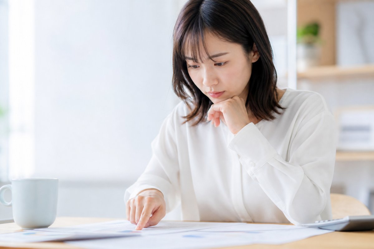 30代の女性がテーブルの上の書類を見ながら、真剣な表情で指先で条件を確認している