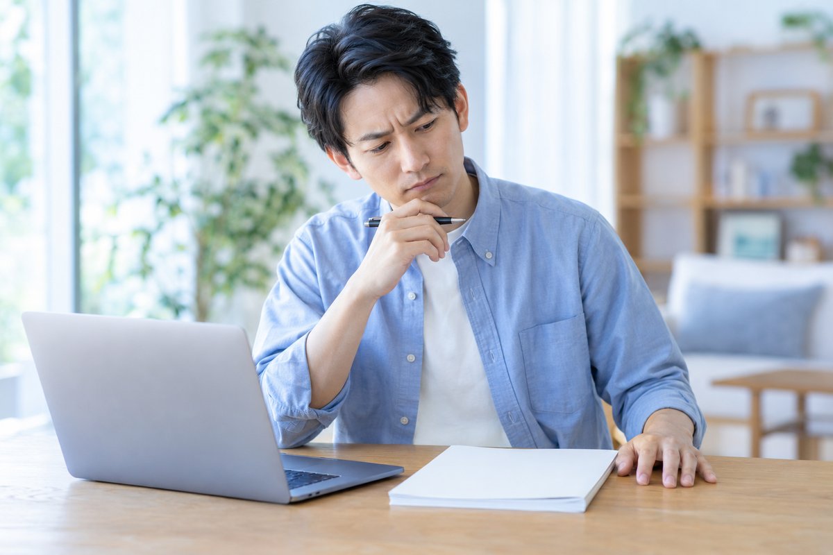 30代の男性が自宅のテーブルでノートパソコンと就業規則の冊子を前に、眉を寄せて困った表情で何から始めるべきか考え込んでいる
