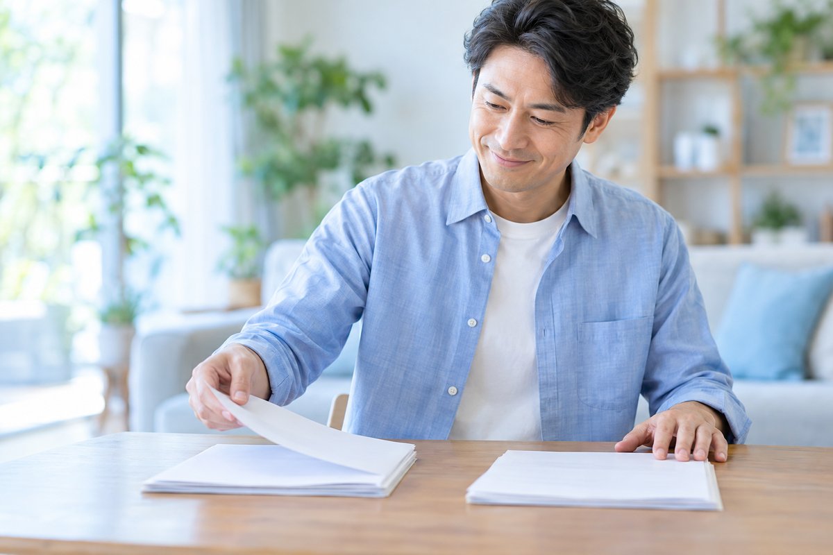 40代の男性がテーブルで書類を2つの束に分けながら、内容を確認して納得した表情を見せている